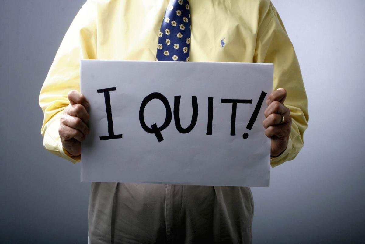A man in a dress shirt and tie holds a sign that says "I quit!"