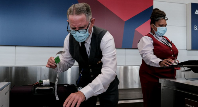 Airline employees check in luggage while wearing face masks