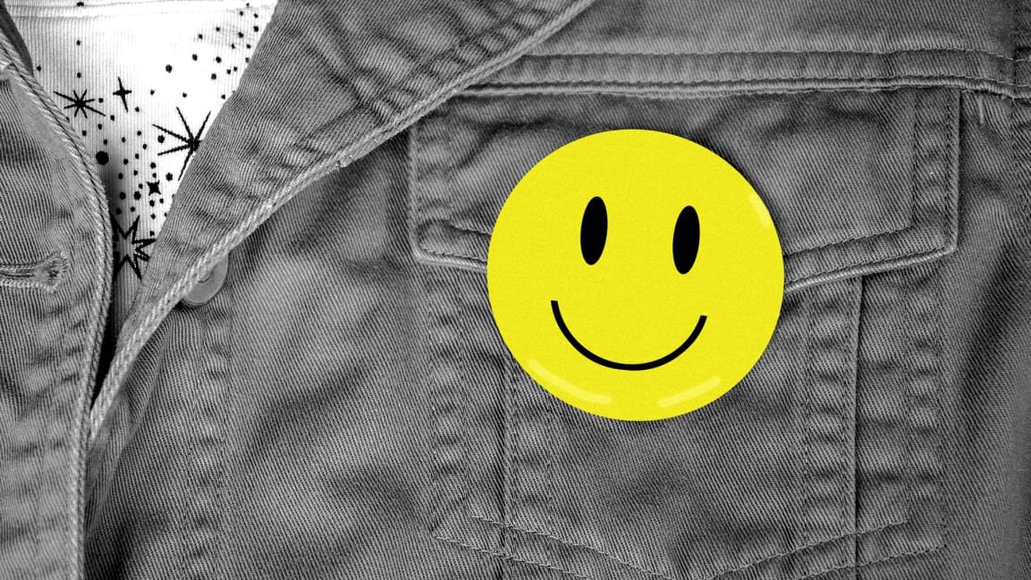 A close-up of a person's jacket shows a smiley face button pinned to the chest