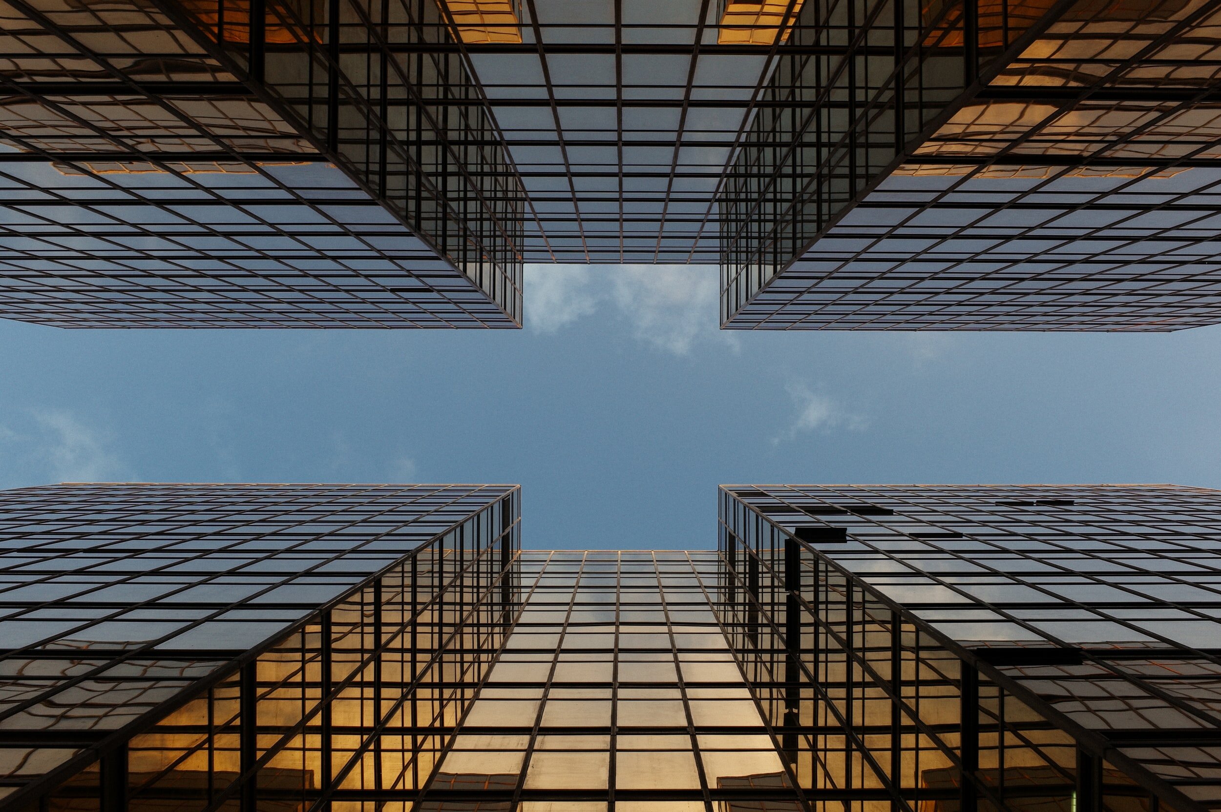 The camera looks directly upward at the sky between two towering glass office buildings