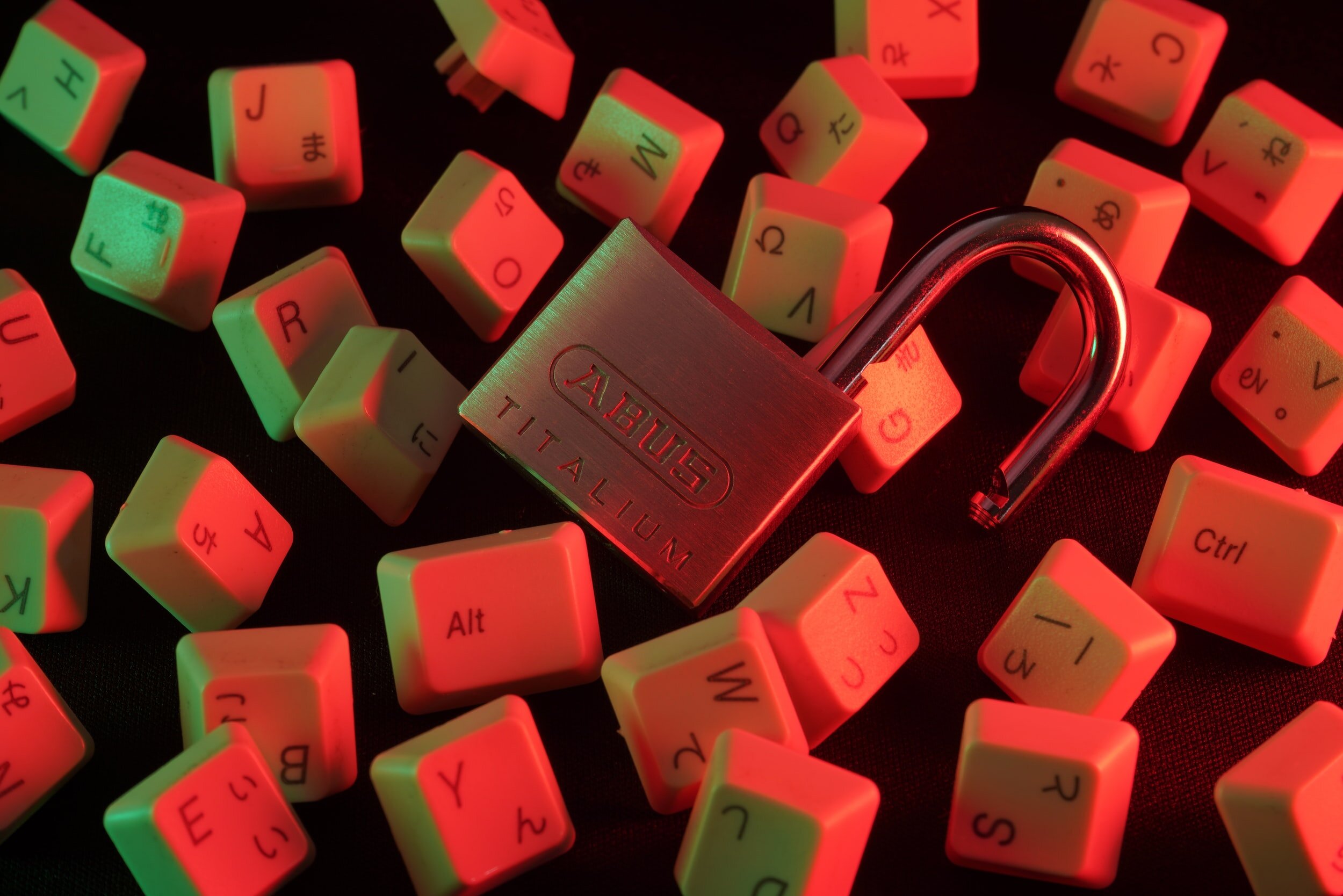An open padlock is surrounded by keyboard keys and bathed in red light