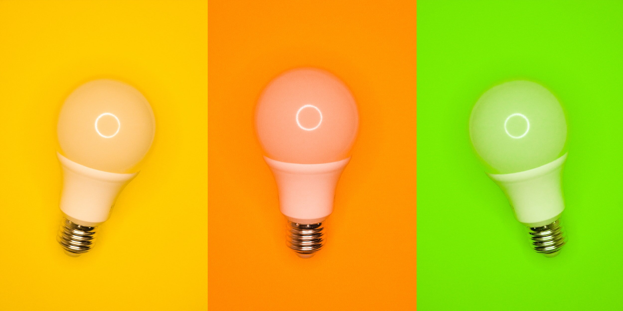 Three lightbulbs in different colors rest against matching backgrounds