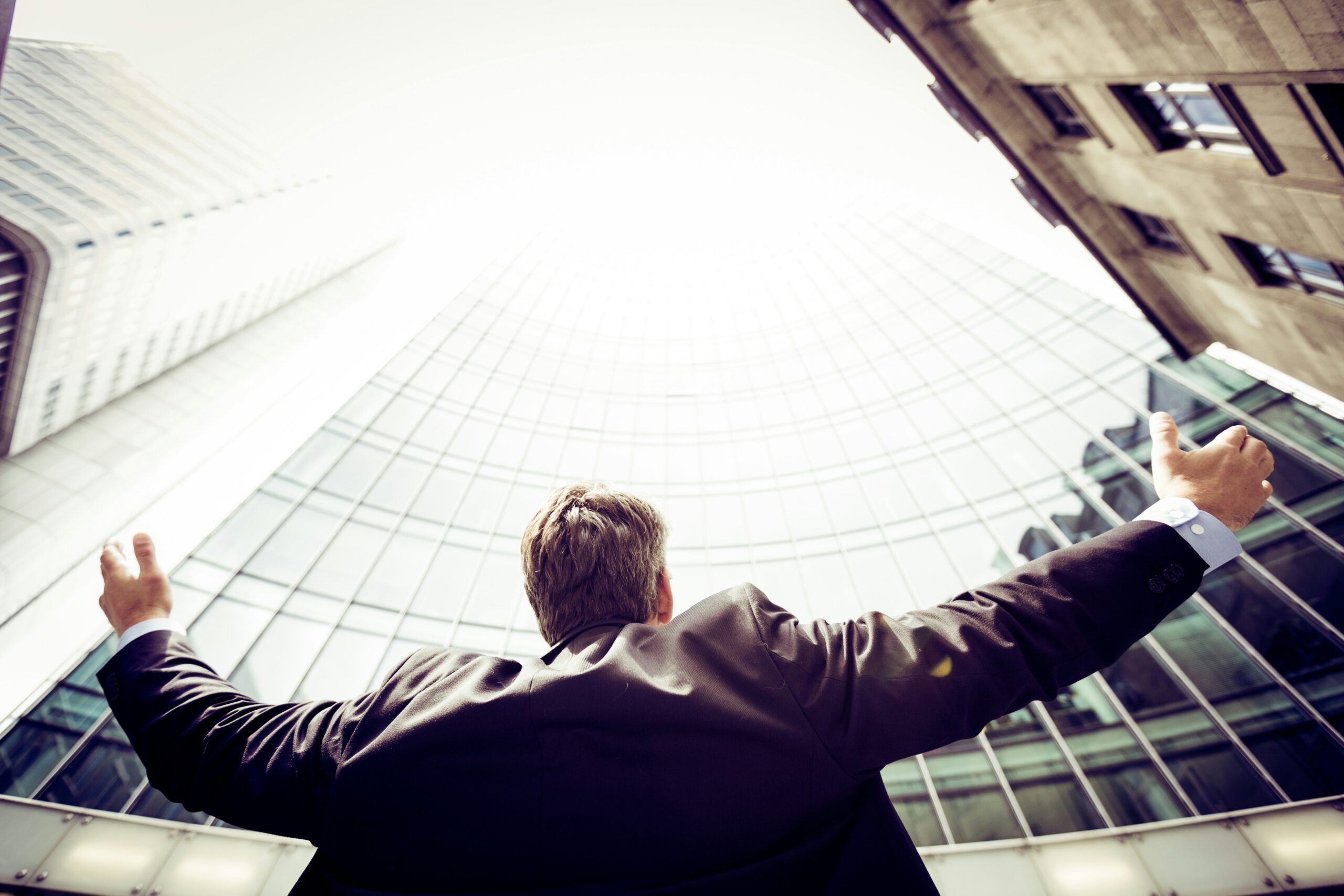 Businessman looking up a skyscraper with arms held wide